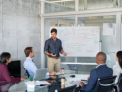 Präsentation eines Mitarbeiters vor einem Whiteboard in einem Teammeeting