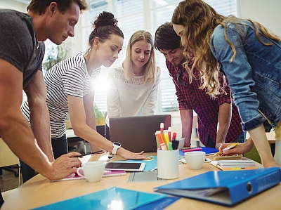 Gruppe von Personen arbeitet gemeinsam an einem Laptop bei einem kreativen Meeting im Büro